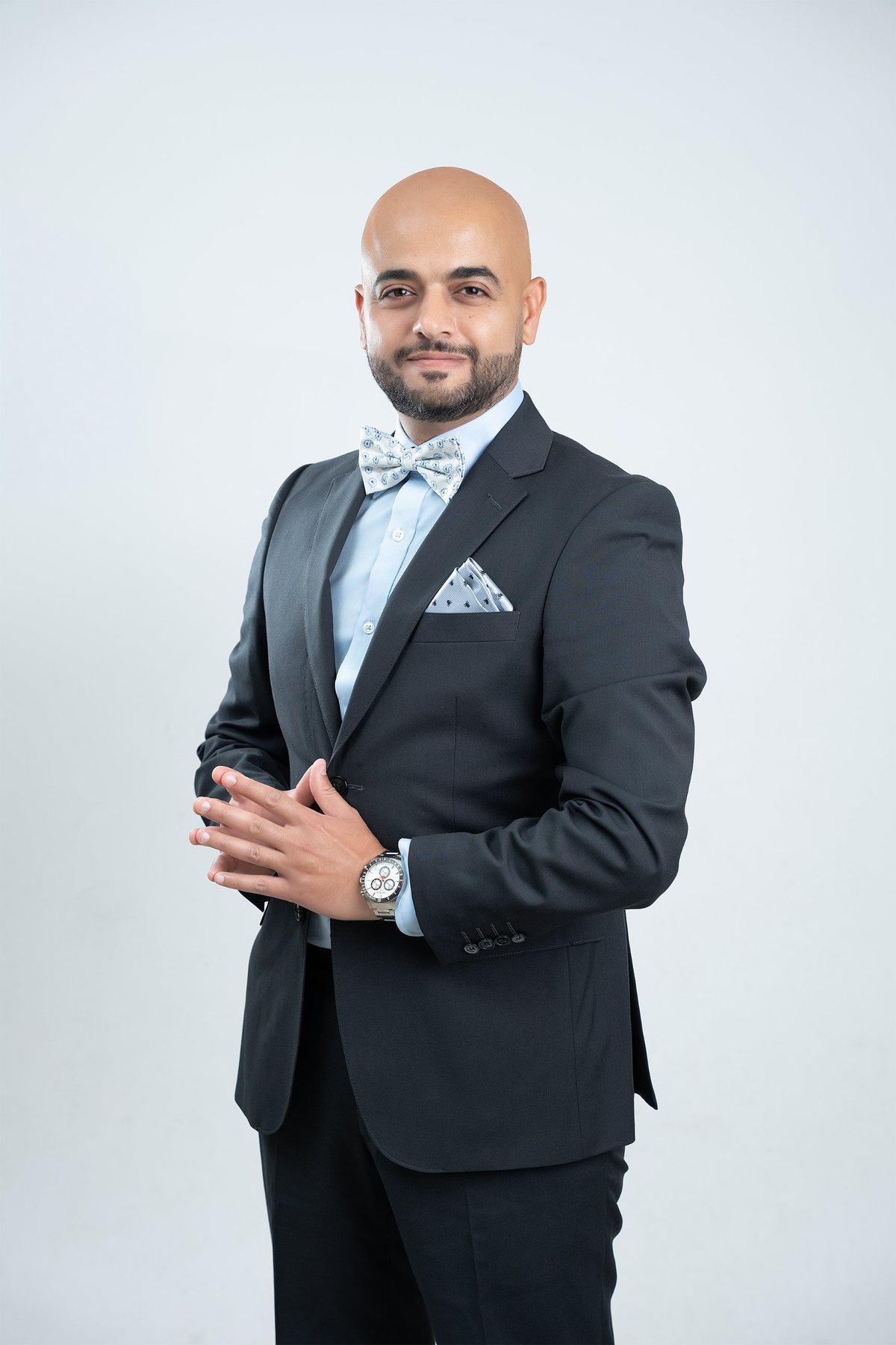 Professional portrait — charcoal suit with pocket square and bow tie, hands steepled, warm confident expression — personal branding photography, Fraser Rise studio