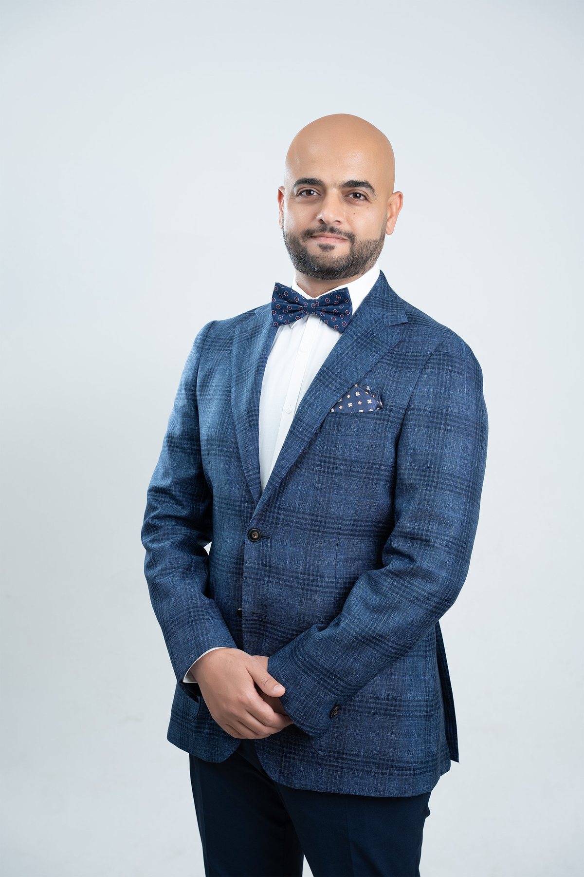 Executive portrait in a blue check blazer, navy bow tie and pocket square, three-quarter pose with hands clasped — corporate headshot photography Melbourne