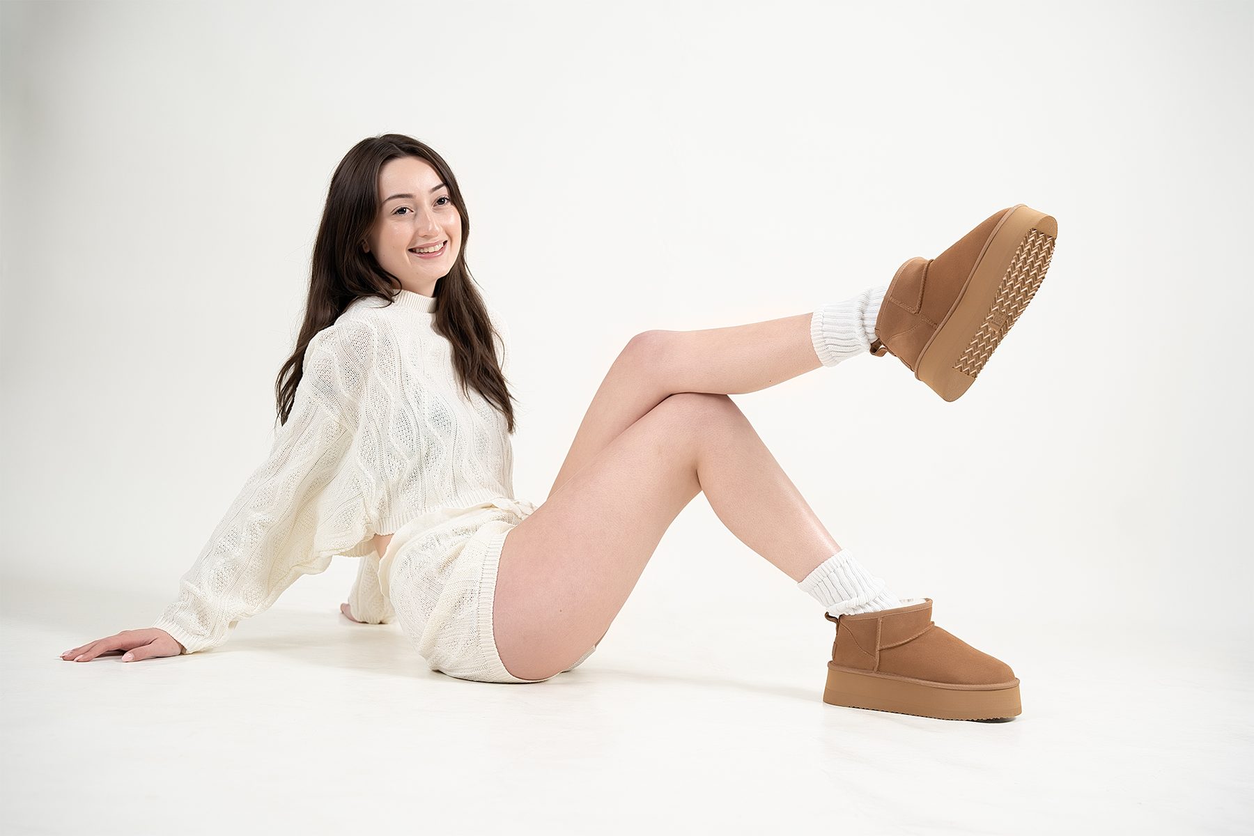 Chestnut platform sheepskin boots on-model, one leg raised, cream knit set and white slouch socks — e-commerce footwear photography