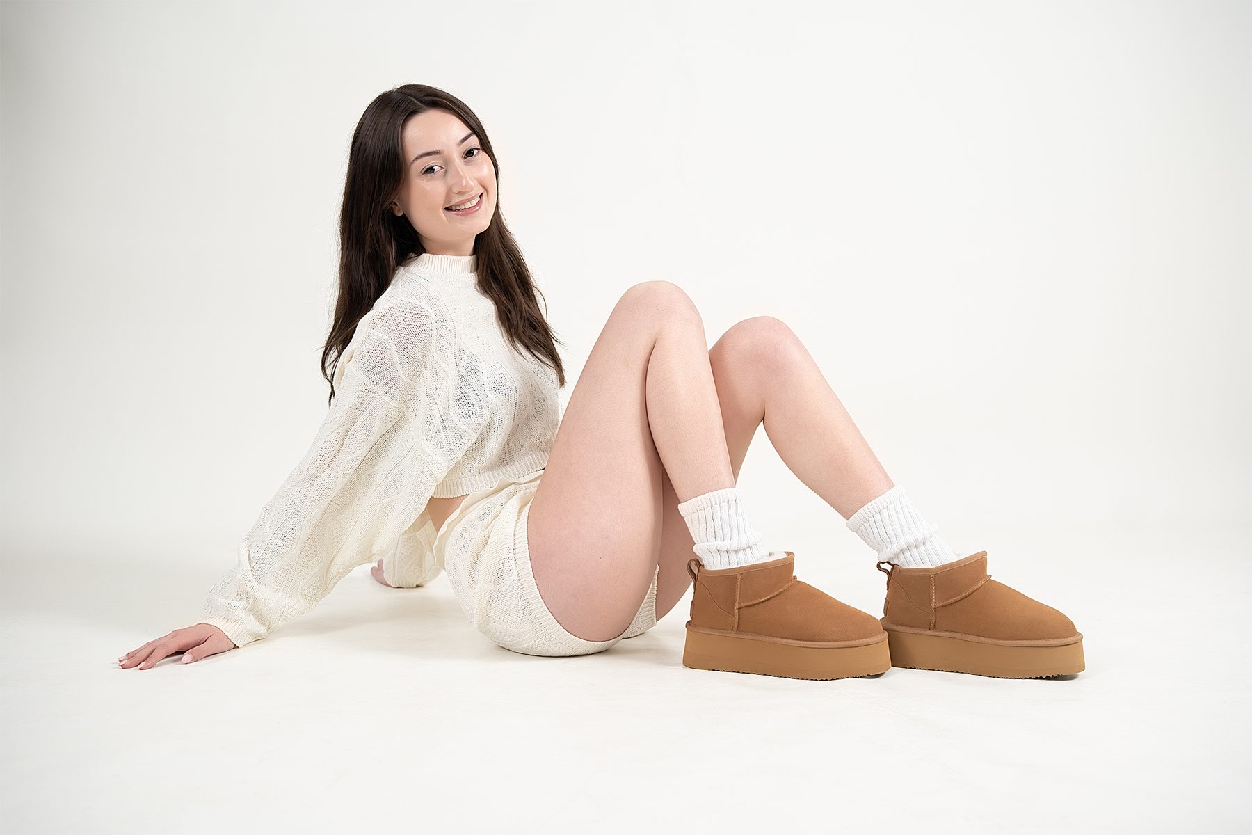 Model seated on the studio floor in chestnut platform boots and white socks, smiling to camera — lifestyle footwear shoot, Fraser Rise studio