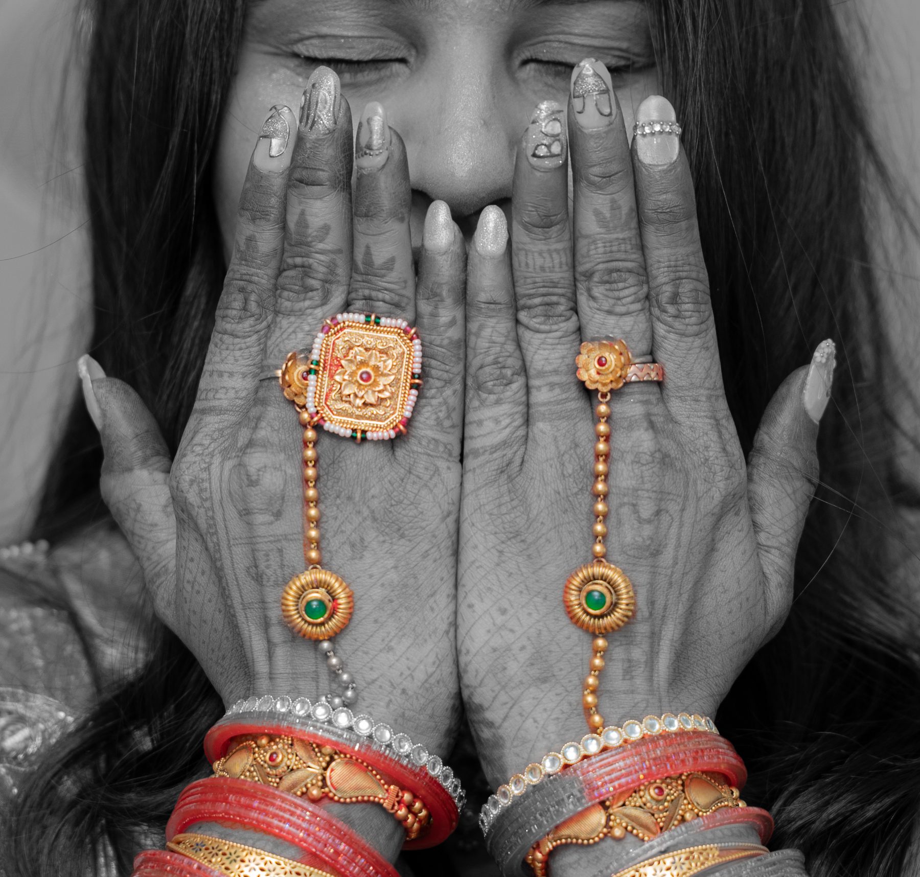 Black and white hands with mehndi, gold haath phool and red bangles covering a smiling face — baby shower detail, Melbourne