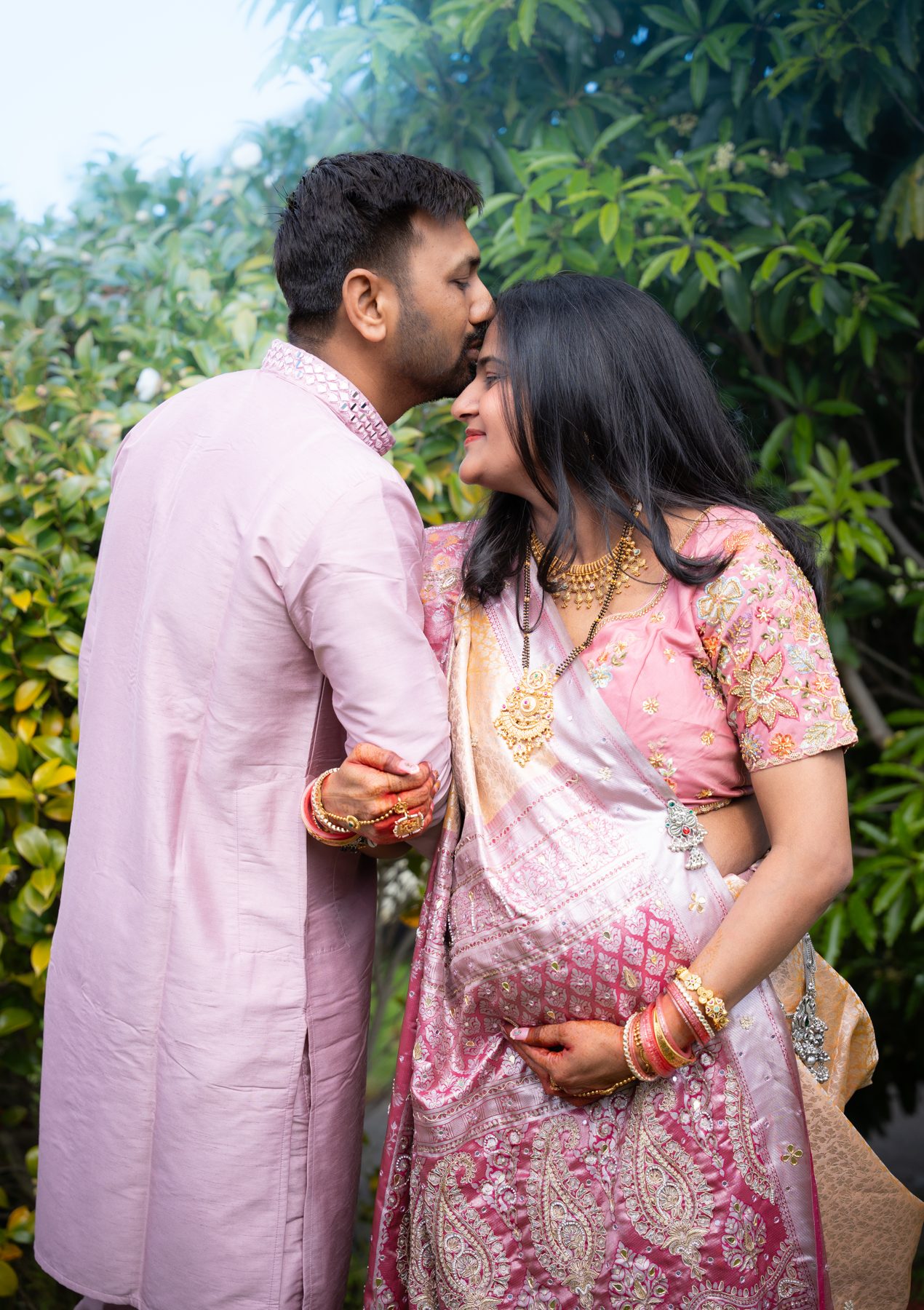Husband kisses his pregnant wife on the forehead, pink silk sari and kurta — baby shower photography Melbourne