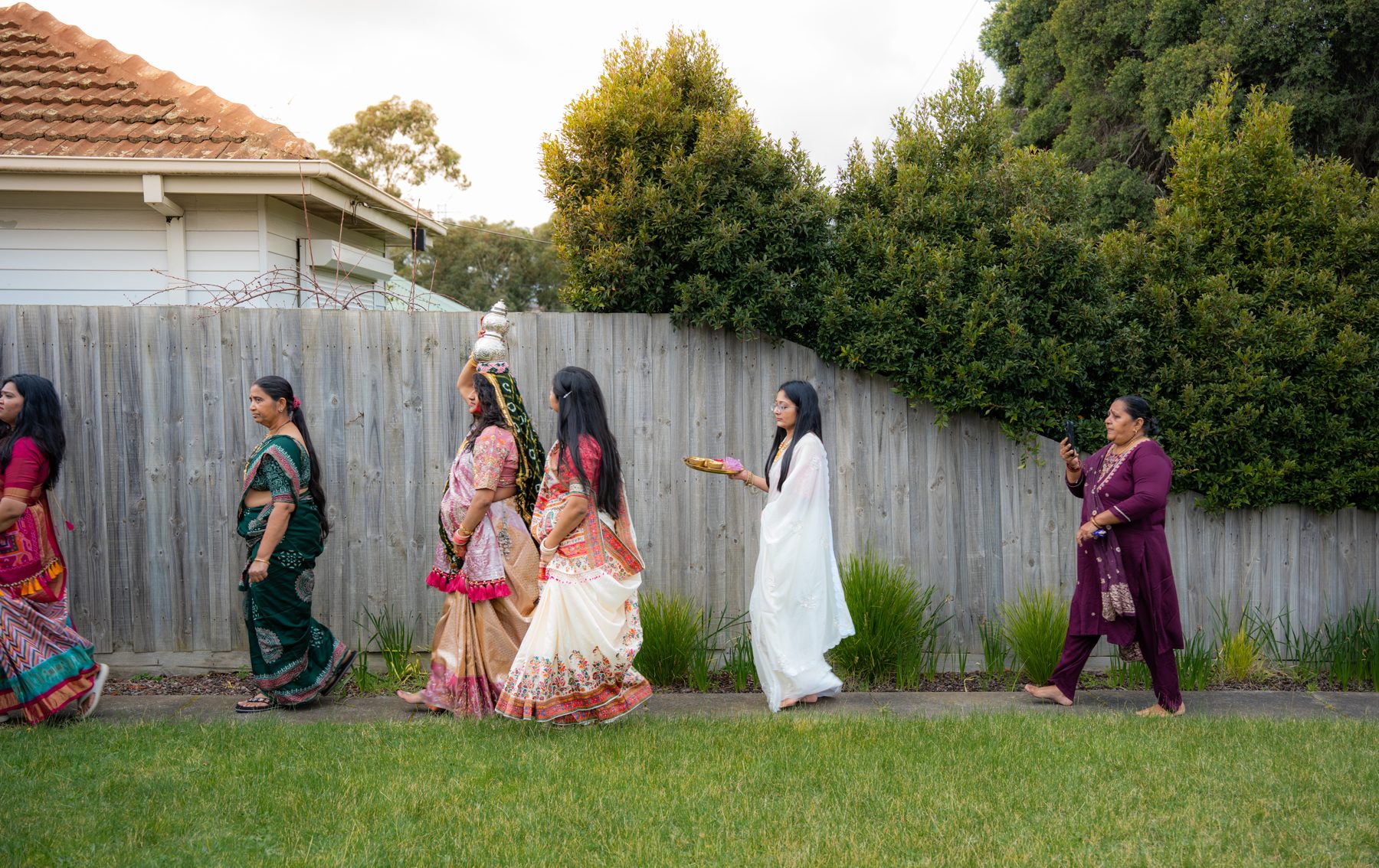 Women in colourful saris walk in procession, the mother-to-be carrying a silver kalash on her head — Godh Bharai photography Melbourne
