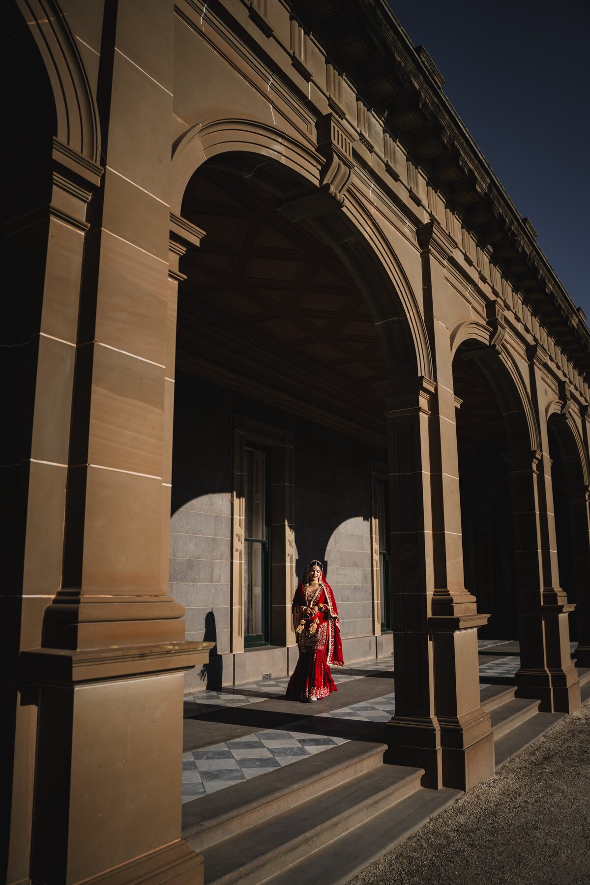 Gradient — Sikh bride walking heritage colonnade, dramatic light