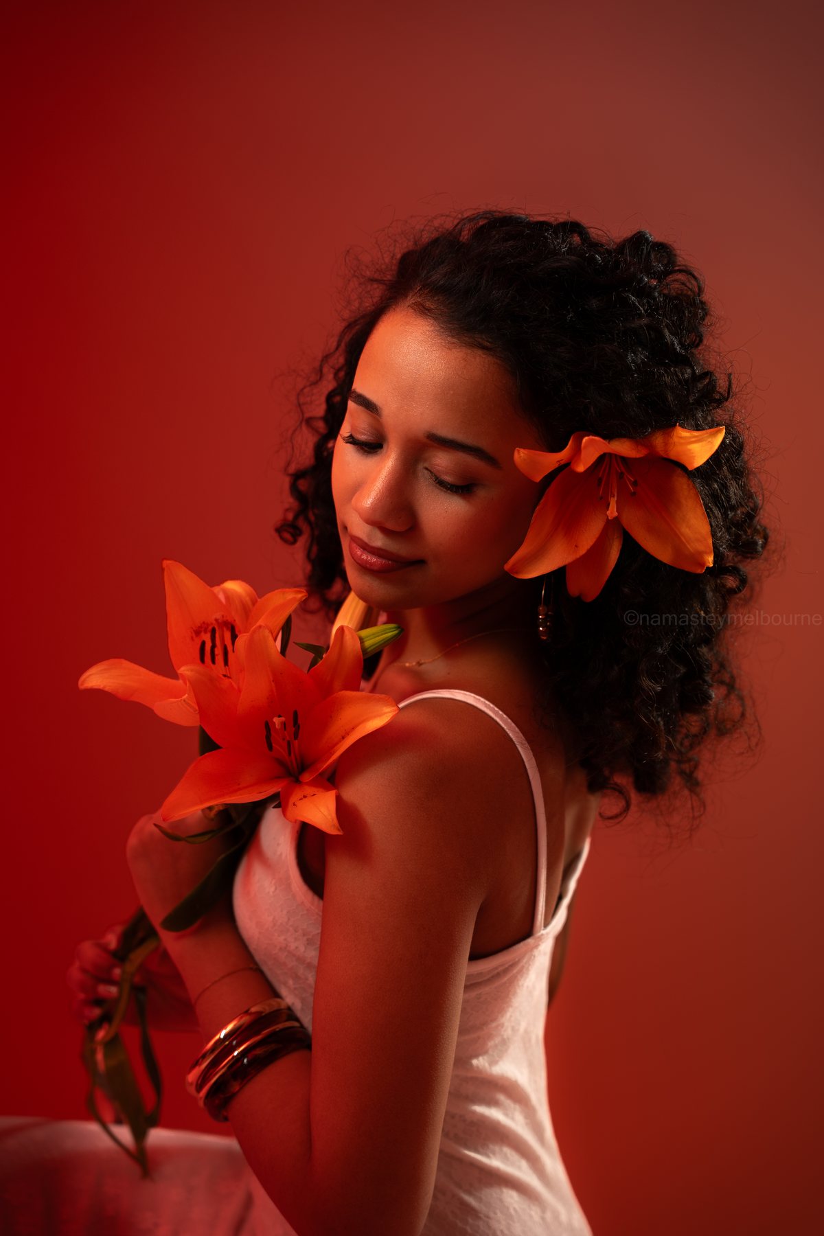 Beauty portrait — orange lilies against a red backdrop, eyes closed, Melbourne studio