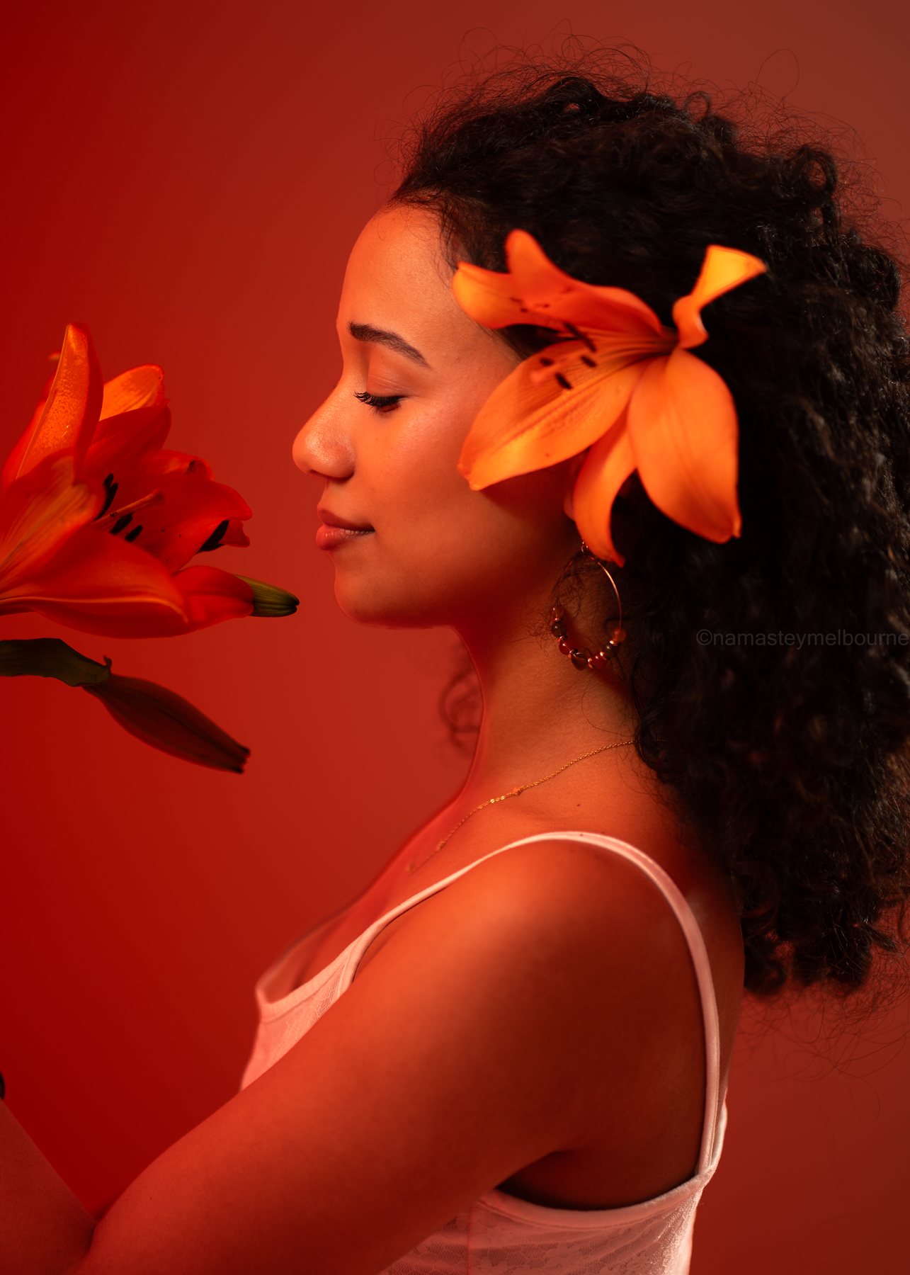 Beauty portrait — profile with an orange lily in the hair against a red backdrop, Melbourne studio