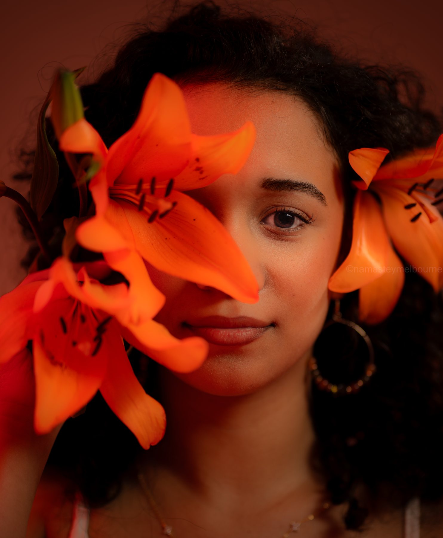 Beauty close-up — orange lily petals across the face, one eye to camera, Melbourne studio