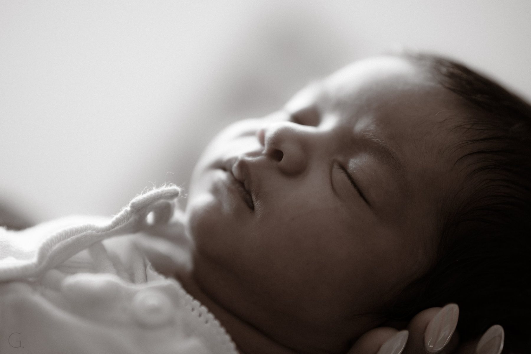 Sepia close-up of a sleeping newborn cradled in her mother's hand