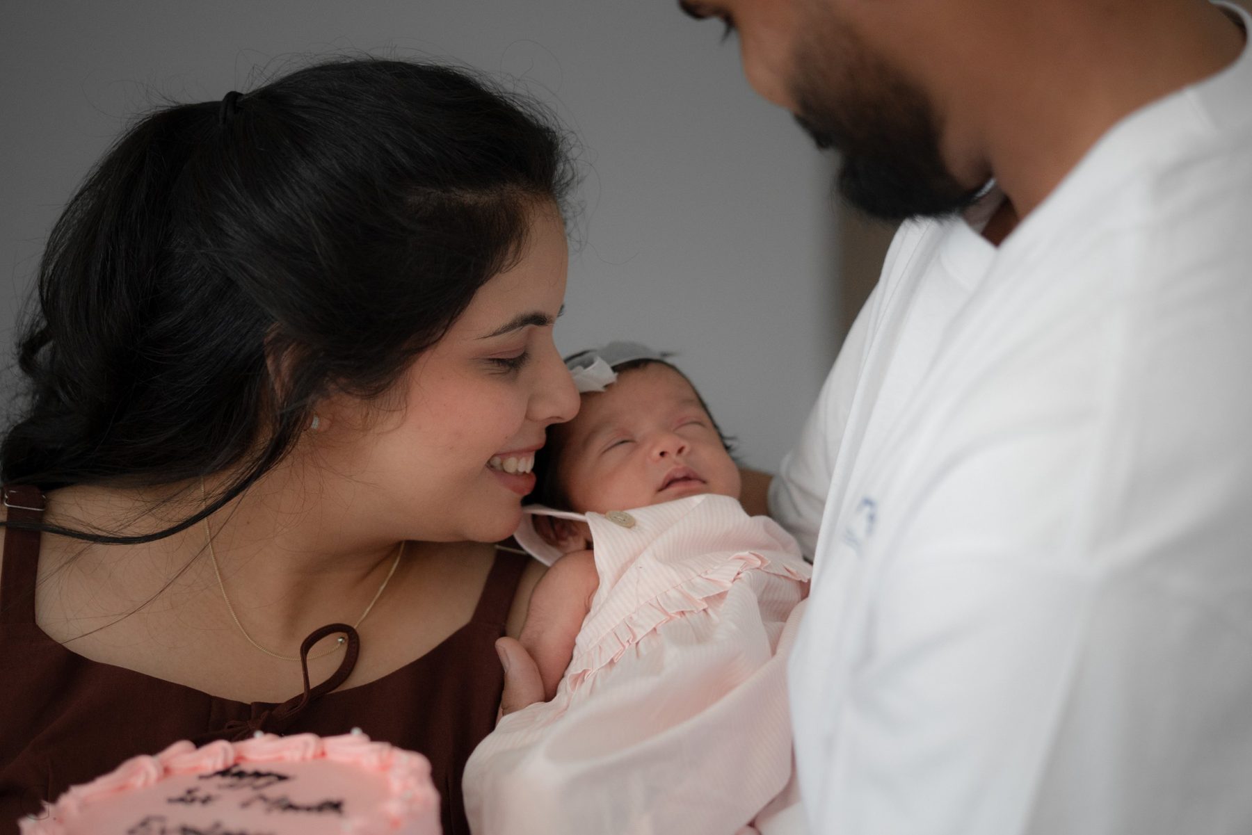 Mother smiling at her sleeping one-month-old as the father looks on — family newborn photography Melbourne