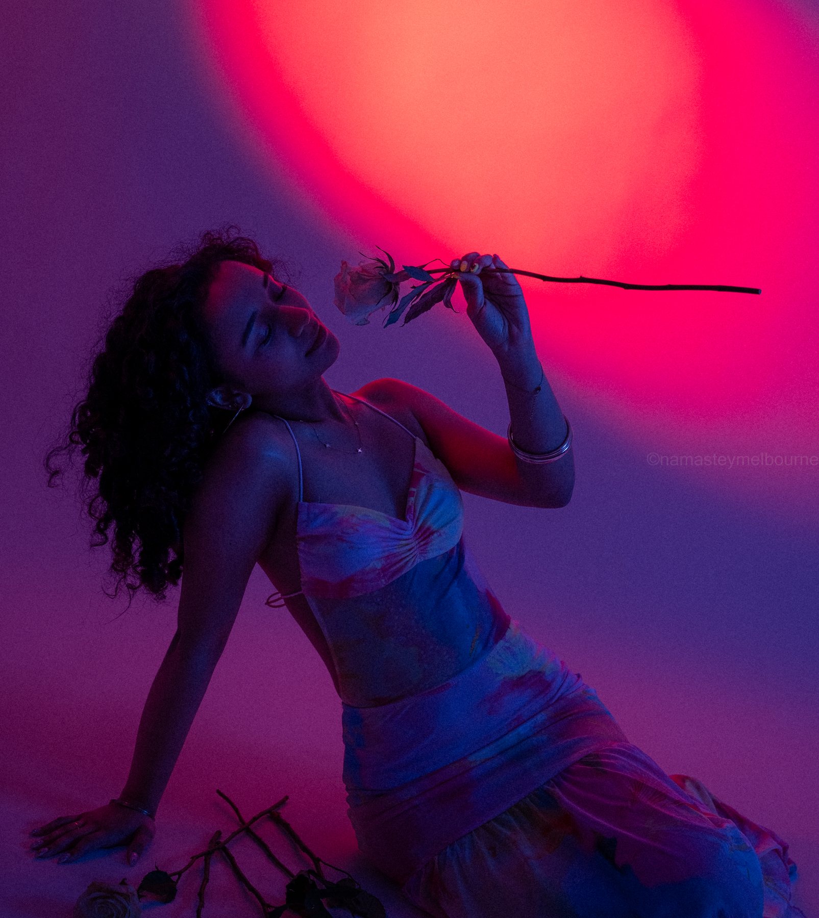 Creative studio portrait — head tilted back, smelling a rose under a pink gel spotlight, Melbourne studio