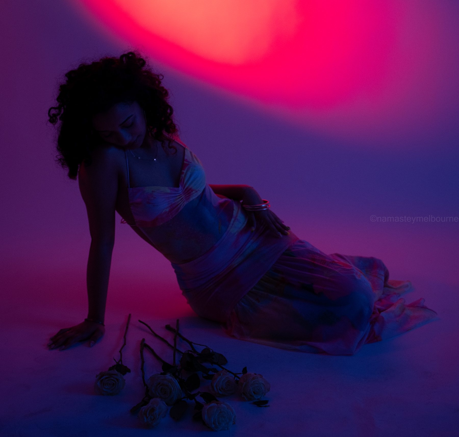 Creative studio portrait — reclining beside scattered white roses under a pink and violet gel spotlight, Melbourne studio